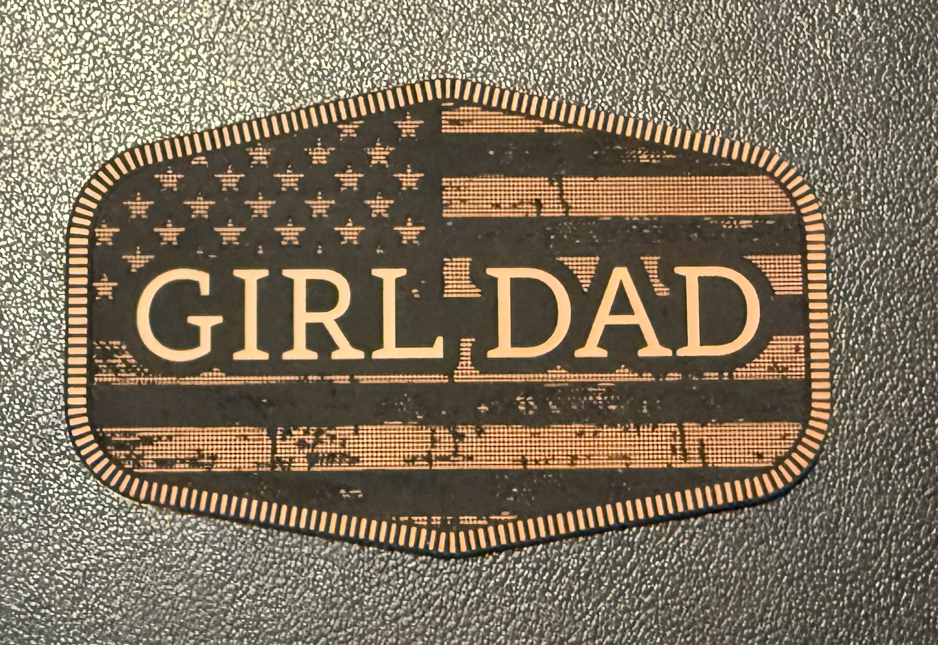 Close-up of a leather Girl Dad patch with patriotic engraved detail.
